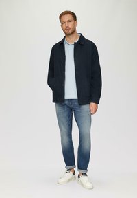 Męska ciemnogranatowa kurtka z guzikami, jasnoniebieski polo i podwinięte dżinsy. Białe trampki z czarnymi akcentami dopełniają strój.