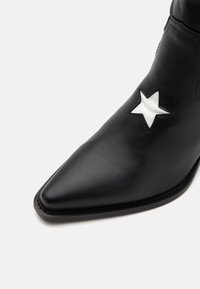 Czarne skórzane botki za kostkę o spiczastym nosku, z białą gwiazdką po boku. Gładka tekstura i przeszycia wzdłuż podeszwy.