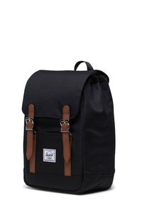 Black canvas backpack with brown leather straps, a front pocket, and a flap closure. Features a logo patch on the front.