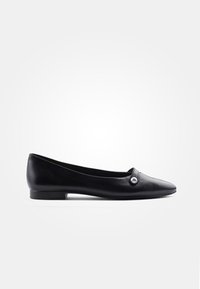 Chaussures plates en cuir noir avec un bout pointu et un petit bouton décoratif. La semelle est discrète et fonctionnelle.