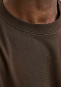 Hnědý bavlněný triko s kulatým výstřihem, hladkou texturou a krátkými rukávy, které má čistý vzhled bez viditelných log nebo vzorů.