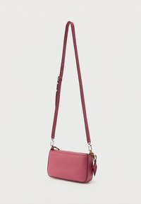 Μικρή ροζ τσάντα χειρός από δερματίνη με υφή, με ρυθμιζόμενο λουρί και ασημένιο εξοπλισμό, κρεμασμένη σε απλό λευκό φόντο.