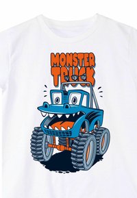 Valkoinen t-paita, jossa on sininen monsteriauton grafiikka, jossa on suuret silmät, terävät hampaat ja liioitellut piirteet. Teksti: "MONSTERIAUTO" oranssilla.