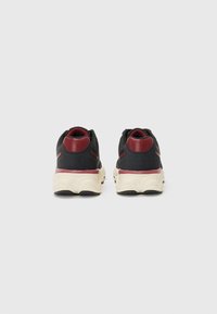Black sneakers with a textured fabric upper, contrasting burgundy heel accents, cream-colored sole, and curved design features.