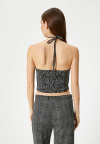 Top corto a rayas blanco y negro con lazo en el cuello. Tejido texturizado con líneas verticales, combinado con pantalones a juego con el mismo patrón.