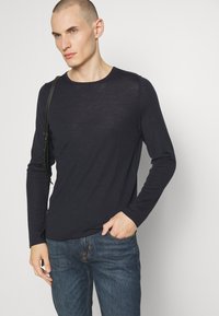 T-shirt a maniche lunghe blu scuro con scollatura rotonda e un tessuto leggermente strutturato, abbinato a jeans in denim blu. Design minimalista.