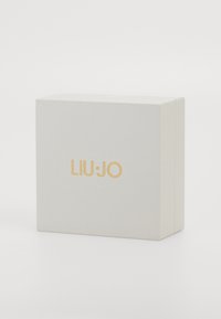 Svetlo šedá textúrovaná škatuľa so zlatým logom "LIU·JO" umiestneným na strede prednej strany, z pohľadu mierne z pravej strany na bielom pozadí.