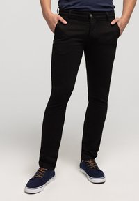 Czarne spodnie z denimu o wąskim kroju i pięciokieszeniowym designie, z zapięciem na guzik i kontrastującymi przeszyciami. Noszone z niebieskimi trampkami.