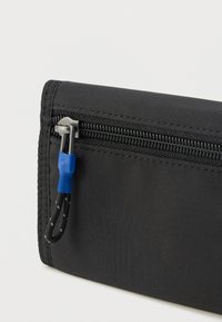 Sort stofpung med en tekstureret overflade, der har en sølv lynlås med en blå trækketag for nem adgang.