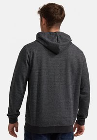 Haut à capuche gris avec un tricot texturé, capuche ajustable et poignets côtelés. Présente un petit logo sur l'épaule gauche et une coupe décontractée.