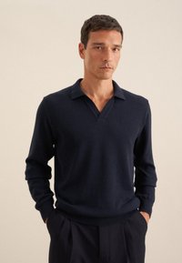 Marineblaues V-Ausschnitt-Pullover aus feinem Strickstoff mit langen Ärmeln und geripptem Saum. Der Kragen hat ein flaches, offenes Design für eine lässige Passform.