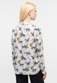 Lange mouwblouse van lichte stof met een speelse patroon van blauwe luipaarden, bloemen en bladeren op een crèmekleurige achtergrond.
