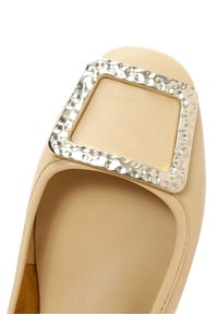 Chaussure plate beige avec bout arrondi et grande boucle carrée argentée texturée à l'avant.