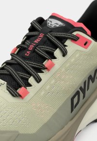 Ανοιχτό πράσινο συνθετικό αθλητικό παπούτσι με διχτυωτό επάνω μέρος, μαύρες και ροζ λεπτομέρειες, υφή επιφάνειας και επισημωμένο λογότυπο "DYNAFIT" στο πλάι.