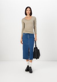 Khaki ribaga pikkade varrukatega särk, millel on laineline kaelus ja pitsaktsendid, kombineeritud denim midi seelikuga, millel on ees lõhik, must kott ja jalanõud.