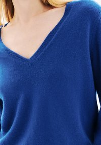 Maglione blu a scollo a V realizzato in un morbido tessuto testurizzato con un taglio rilassato. Il colletto è ben definito e il materiale appare leggero.