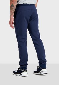 Marineblauwe trainingsbroek met een gladde textuur, taps toelopende benen en zijzakken, gecombineerd met donkere sneakers met witte zolen en zwarte veters.