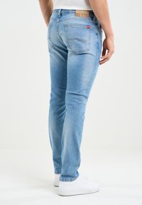 Gaiši zili slim-fit džinsi ar nedaudz nolietotu tekstūru, piecu kabatu dizains un zīmola ādas uzlīme aizmugurējā jostas vietā.