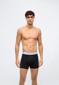 Svarta bomullsboxershorts med ett grått elastiskt midjeband märkt "Calvin Klein", med en tajt passform och slät textur.