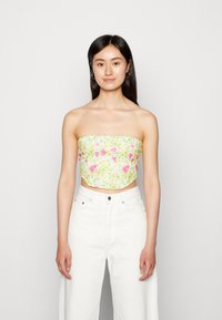 Top crop sem alças em estampado floral verde claro, apresentando flores rosas e amarelas. Combinado com calças largas de cintura alta brancas.
