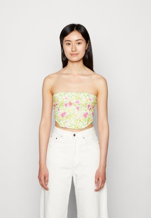 Top crop sem alças em estampado floral verde claro, apresentando flores rosas e amarelas. Combinado com calças largas de cintura alta brancas.
