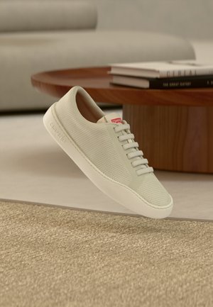 Hvid sneakers med mesh-overdel, tekstureret overflade og flad gummisål. Har seks snørehuller og en lille rød logotab nær tungen.