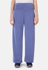 Helllila, locker sitzende Jogginghosen mit einem breiten Bund und weicher Textur. Kombiniert mit blauen Sportschuhen.