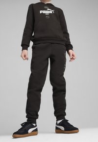 Černá bavlněná mikina s bílým logem Puma, spárovaná s černými tepláky s jemnými detaily. Černé tenisky s bílou a gumovou podrážkou.