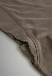 Ruskea kangas, jossa on sileä pinta, poimutetut reunat ja hieman ryppyinen ulkonäkö, esittelee kerroksellisen reunadetaljin.