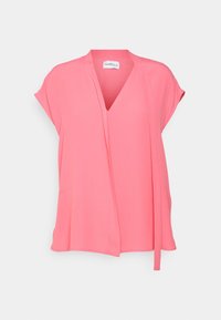 Lyserød bluse med korte ærmer, V-hals og løs pasform, med en lang stofsløjfe på den ene side, på en ensartet lys grå baggrund.