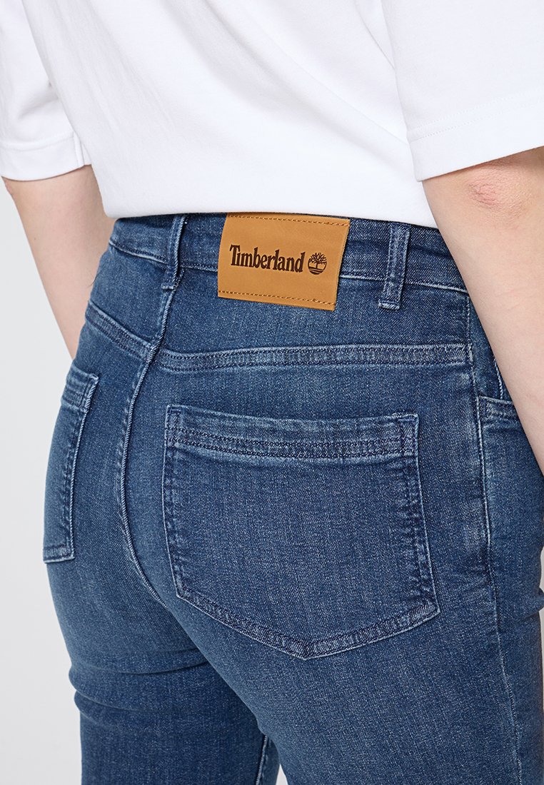Ciemnoniebieskie dżinsy o dopasowanym kroju, z skórzaną łatą z logo Timberland na tylnej części pasa i minimalnymi detalami.