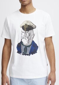 Balta kokvilnas T-krekls ar grafiku, kurā ir zivs jūrnieka cepurē un pīpē, tērpta zilā žaketē un svītrainā kreklā, ar tekstu "Mr. Deep Sea".