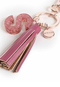 Llave de flecos rosa con un charm de purpurina rosa en forma de 'S', hardware en tono oro rosado, materiales en capas y una etiqueta circular marcada con "MIRIAD."