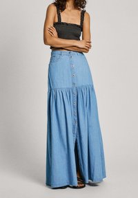 Jeansmaxiklänning i ljusblått med knapprad fram, lagerdesign och en något utsvängd fåll. Mjuk textur med volangdetaljer.