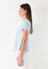 Lyseblå kortærmet T-shirt, blødt stof, afslappet pasform, buet søm, sideslids nederst, med synlige syninger.