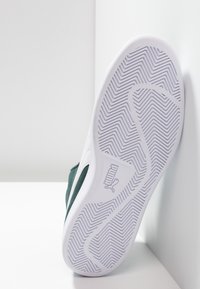 Zelená sneakers s bílou gumovou podrážkou a vzorem rybí kosti. Má hladký textilní svršek a obsahuje značku Puma na boku.