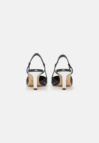 Chaussures à talons hauts en cuir noir avec un talon argenté brillant, dos ouvert et sangles ajustables comportant de petites découpes rondes.