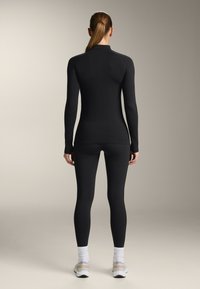 Fekete, hosszú ujjú, testhezálló felső és leggings rugalmas anyagból, sima textúrával és minimális dizájnnal, bordázott részletekkel.