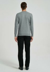 Pull gris à manches longues en tissu doux avec un col rond, porté avec un pantalon noir, vu de dos. Texture lisse et design ajusté.