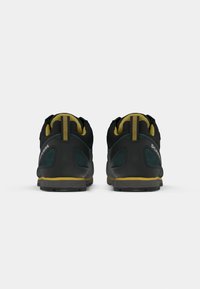 Čierne a zelené turistické topánky s žltými akcentmi, ktoré majú textúrovaný materiál, zosilnenú pätu a drsnú podrážku.
