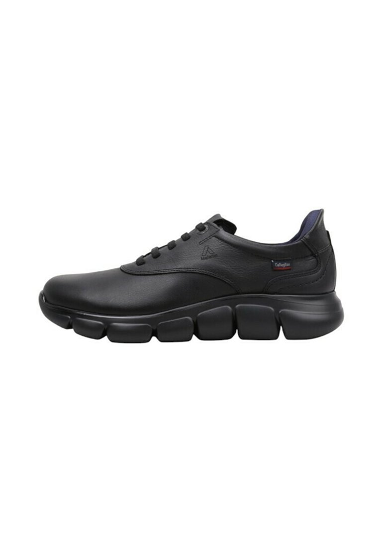 Zapatilla deportiva de cuero negro con un empeine suave, puntera redondeada y suela segmentada distintiva. Cuenta con cordones y un sutil logotipo en el lateral.