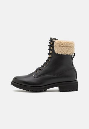 Czarne skórzane buty za kostkę z brązowym sztucznym futrem na kołnierzu, metalowymi oczkami i solidną gumową podeszwą. Posiadają wzmocnione szwy i pętelkę do zakładania.