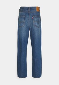 Mörkblå jeans med rakt ben-design, som har en läderlapp bak, två bakfickor med sömdetaljer och en slät yta.