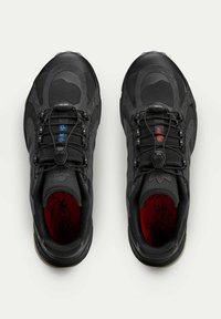 Black athletic shoes with a textured surface, featuring contrasting accents in red and blue, and a secure lace system. Inside has a patterned red insole.
