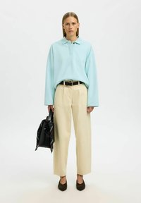 Hellblauer übergroßer Pullover mit Kragen, cremefarbene Hosen mit weitem Bein und dunkelbraune spitze Ballerinas. Schwarze Tasche mit gemustertem Schal-Detail.