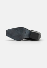 Suela de zapato de cuero negro con una superficie lisa y texturizada que presenta un sutil logotipo. Talón elevado con una parte delantera ancha y plana.