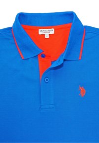 Modrá polo košile s oranžovým límcem a lemem, obsahující dva knoflíky a na levé hrudi vyšívané logo v oranžové barvě. Viditelná velikostní etiketa.