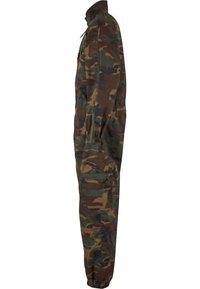 Zöld, barna és fekete árnyalatokban készült kamuflázs overál; elülső cipzárral, rugalmas mandzsettákkal és több zsebbel rendelkezik a funkcionalitás érdekében.