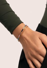 Guldarmbånd med lag på lag af farverige perler. Indeholder blå, pink og grønne sten med en glat tekstur og varierede størrelser.