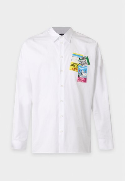 Chemise blanche à manches longues boutonnée avec des écussons graphiques colorés de tickets de remontée mécanique sur la partie gauche de la poitrine.